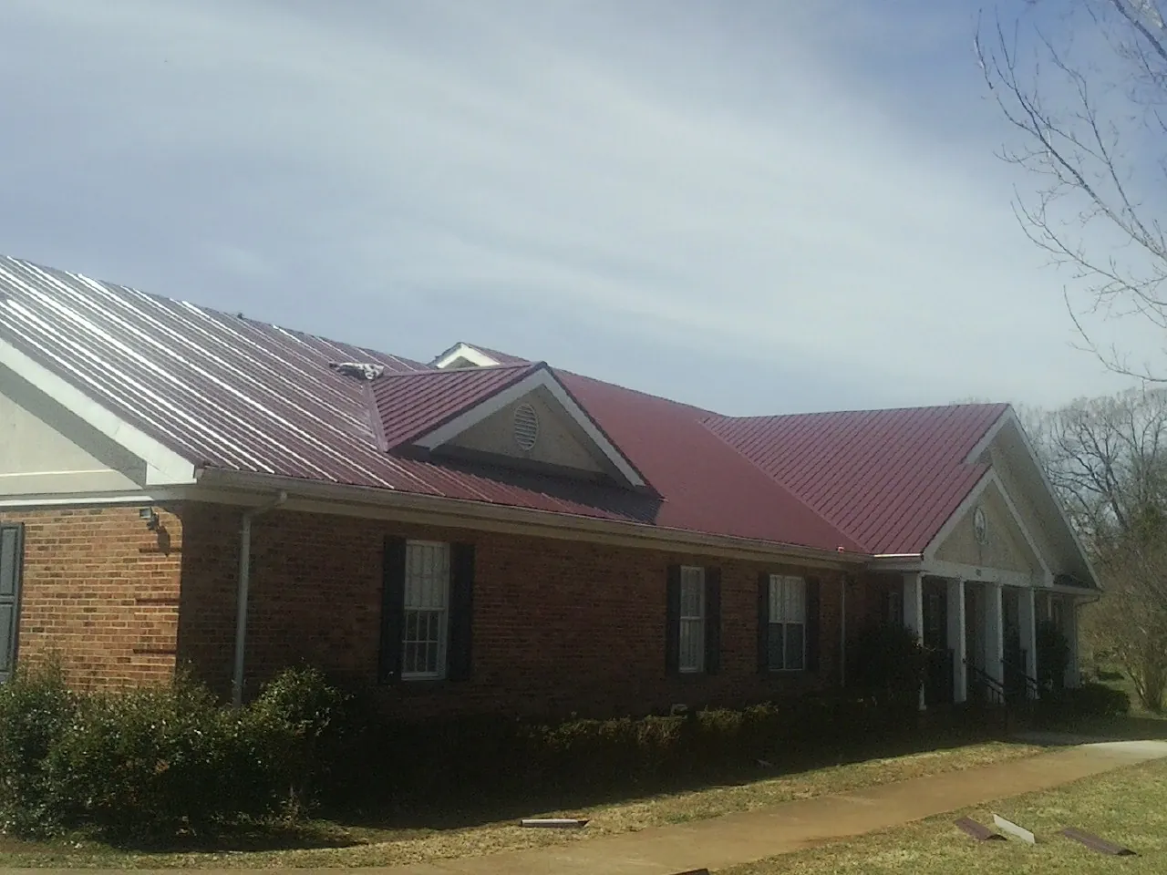 Red metal roof with gabled entries on a long brick building, from a Hail Damage Roof Repair job in Rogersville