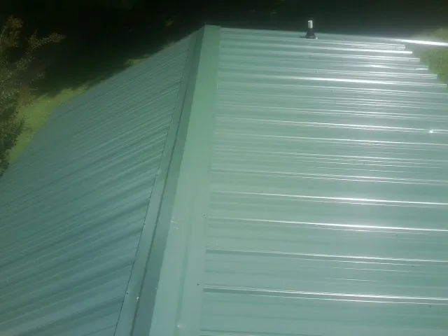New green metal panels meeting at the ridge of a roof — Flat Roof Repair work by our crew in Rogersville