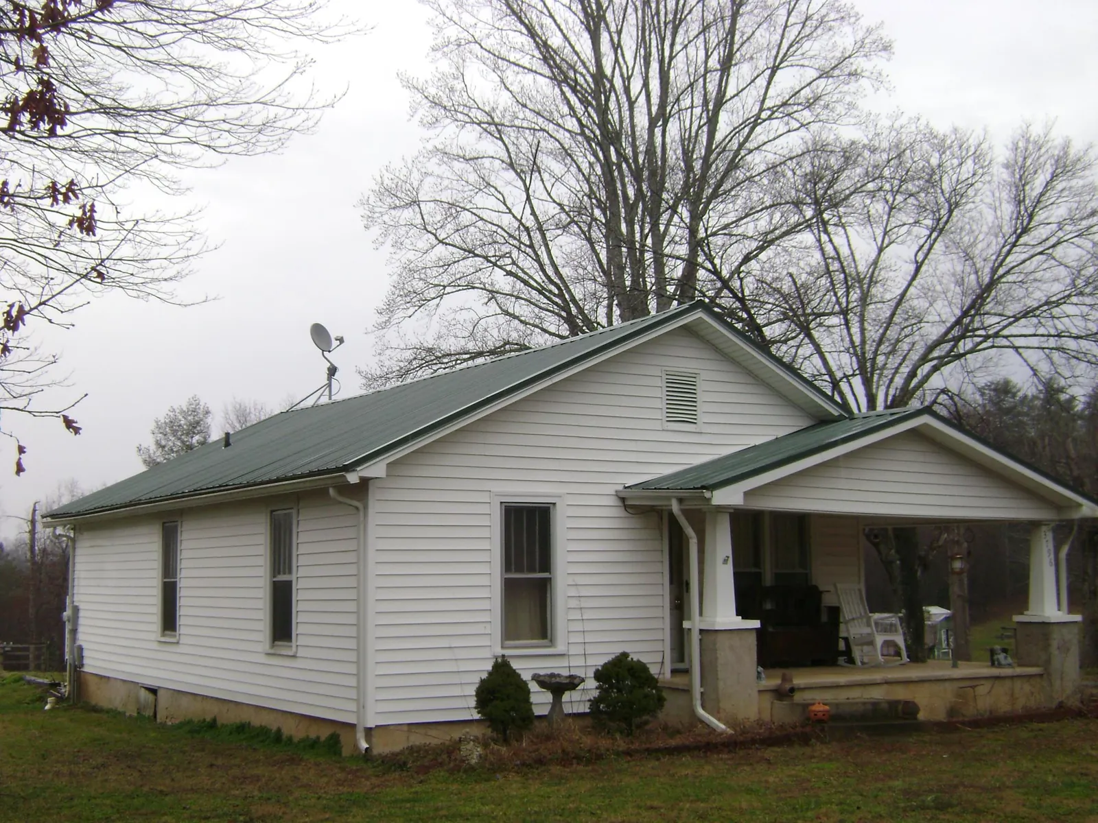 Green metal roof on a white bungalow with a side porch in Rogersville