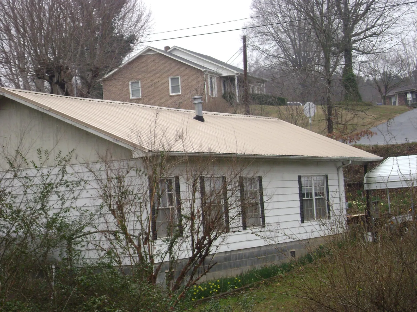 Tan metal roof on a white sided house set into a hillside — Commercial Roofing by Roofing Brothers in Rogersville